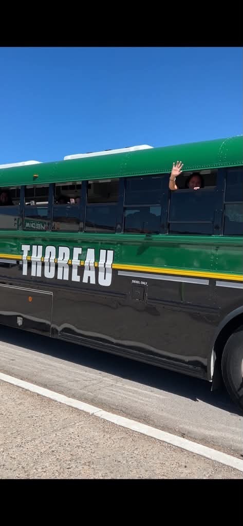A bus with "THOREAU" written on it drives on a road under a clear blue sky.