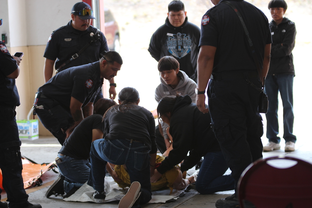 Emergency personnel attend to injured individuals on the floor; two people lie on their backs receiving aid.