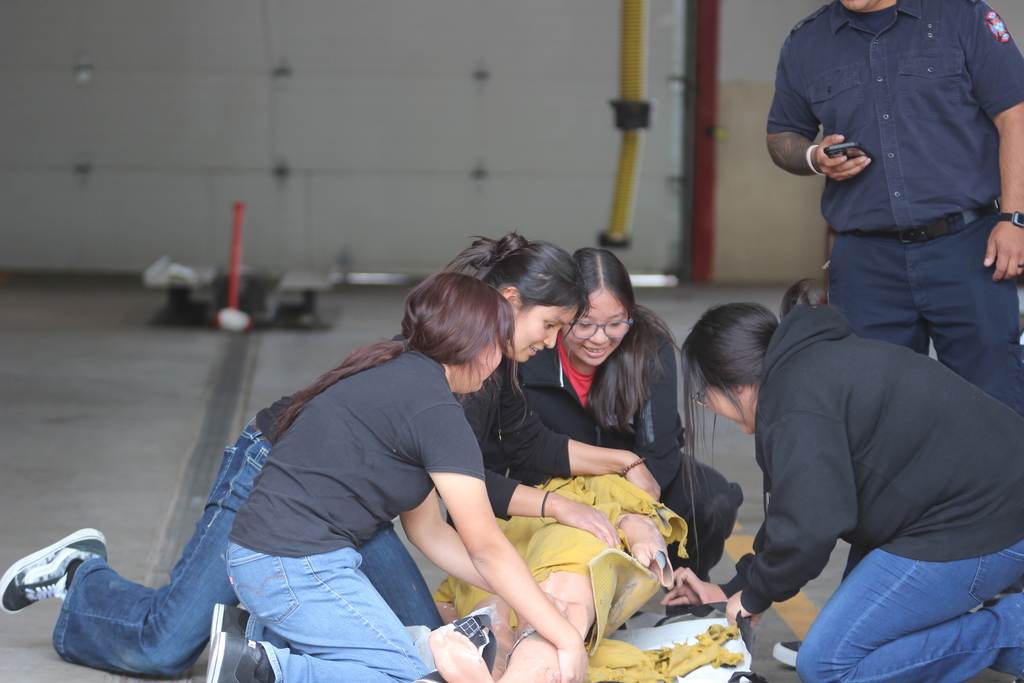 Four individuals are kneeling on a floor, two of them wearing glasses, working on a yellow object.