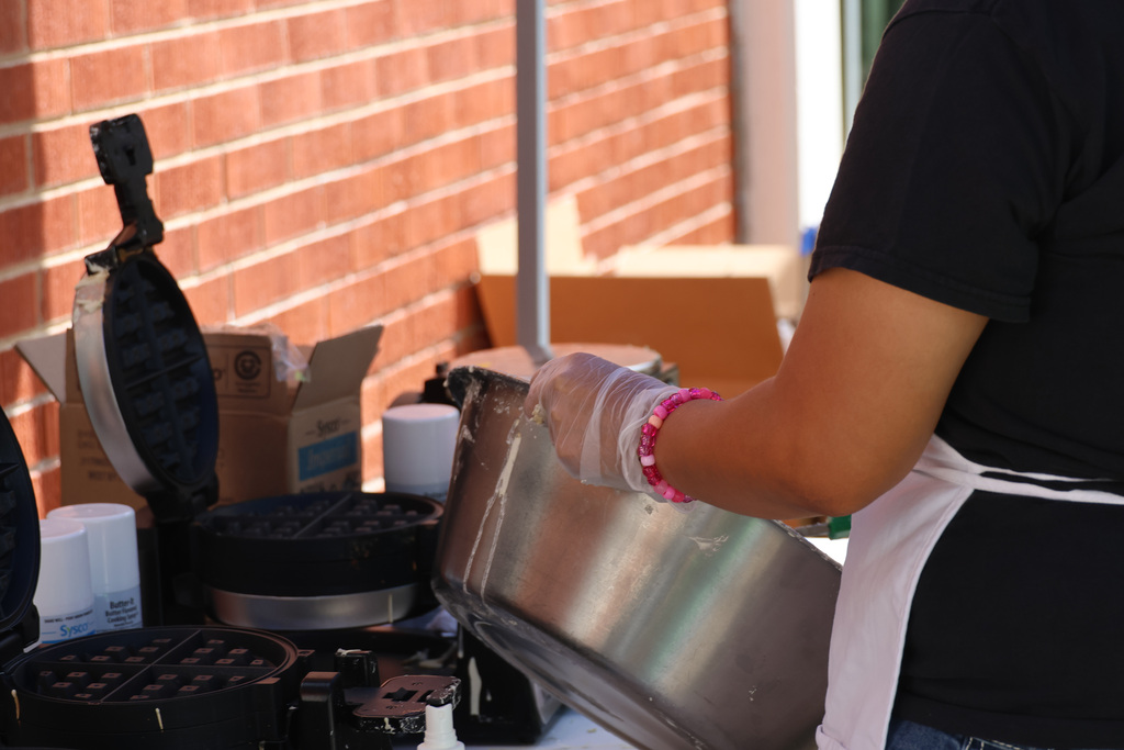 A person in a black shirt, white apron, and gloves prepares food in a kitchen area.