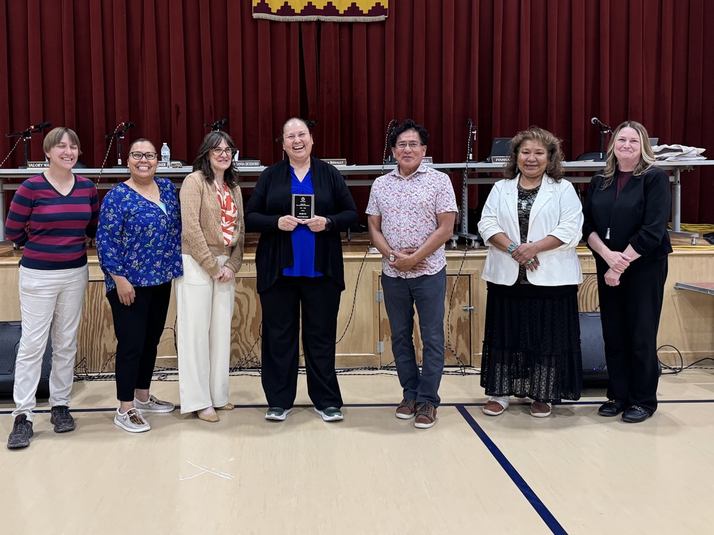 A group of people in a classroom, with one individual holding a trophy. The floor has a blue line.