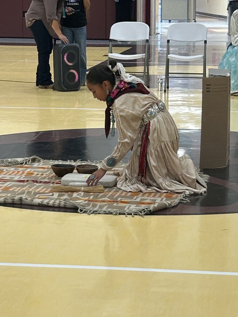 a student in traditional garment is kneeling down with a basket in the gyn