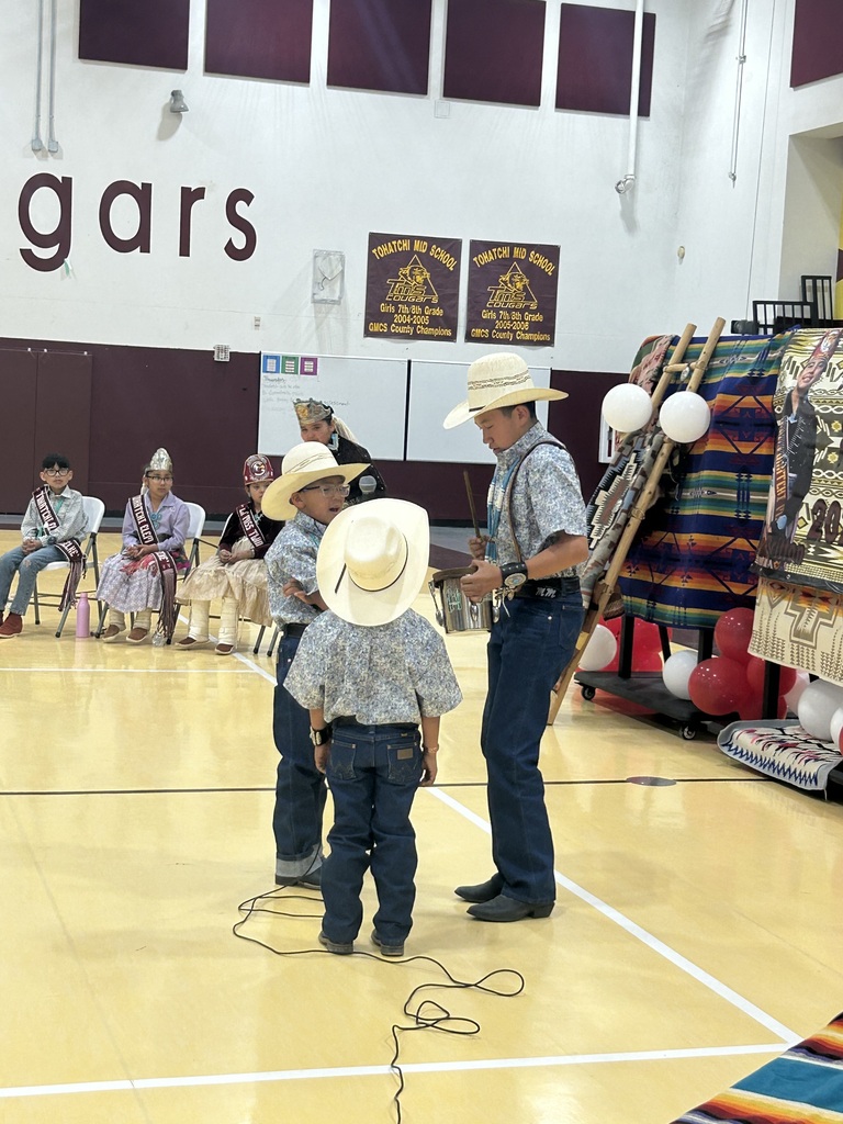 three students dressed in jeans and cowboy hats stand in a circle in the gym