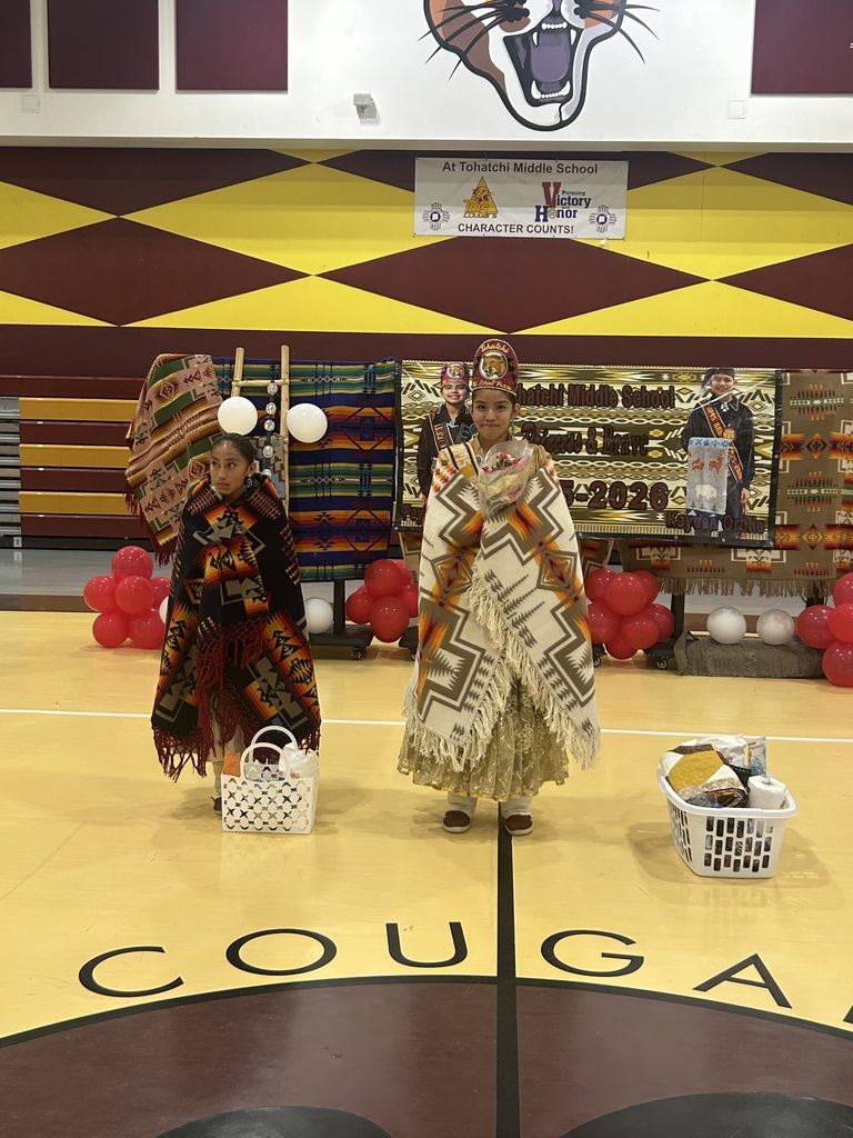 two girls in traditional outfits wrapped in blanket in a gym.