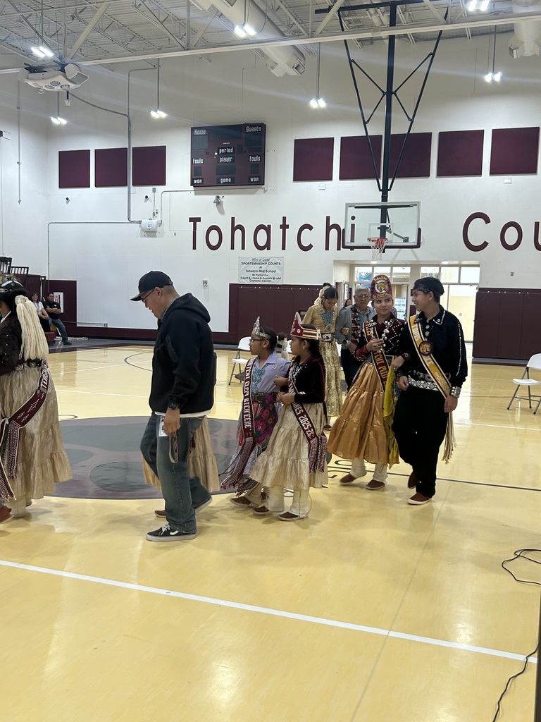 students in traditional garb are in pairs waliking in a circle in the gym