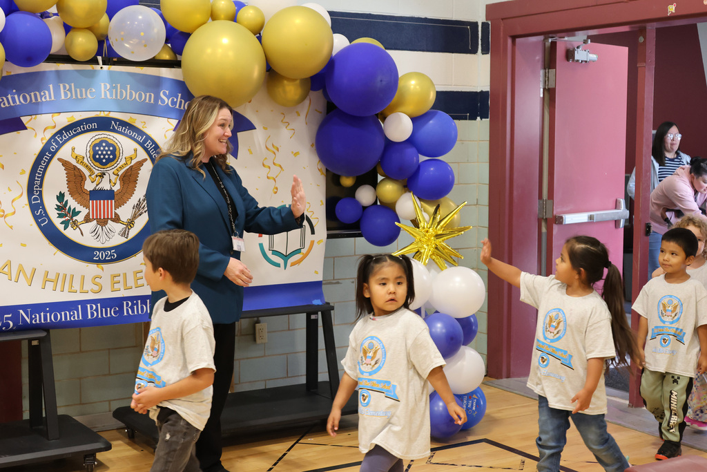 A woman and four children are in a room with balloons. The children are wearing white shirts.