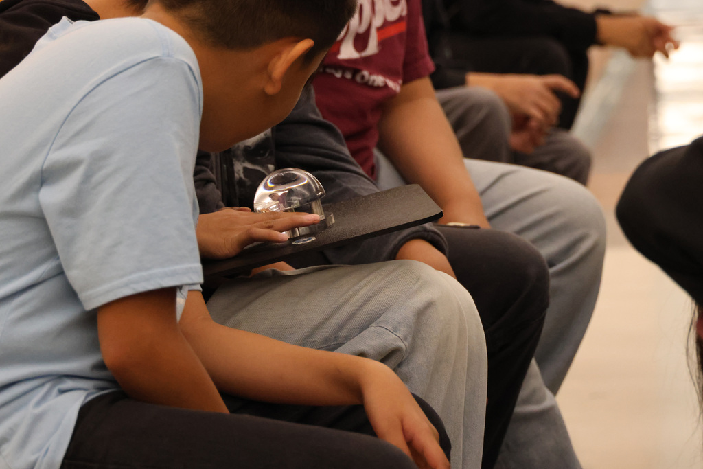 A boy in a blue shirt is looking at a clear glass object held by another person in front of him.