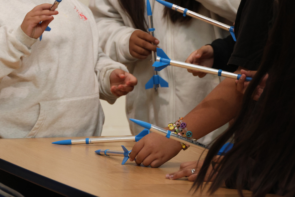 Several people wearing white hoodies gather around a wooden table with blue and silver objects.