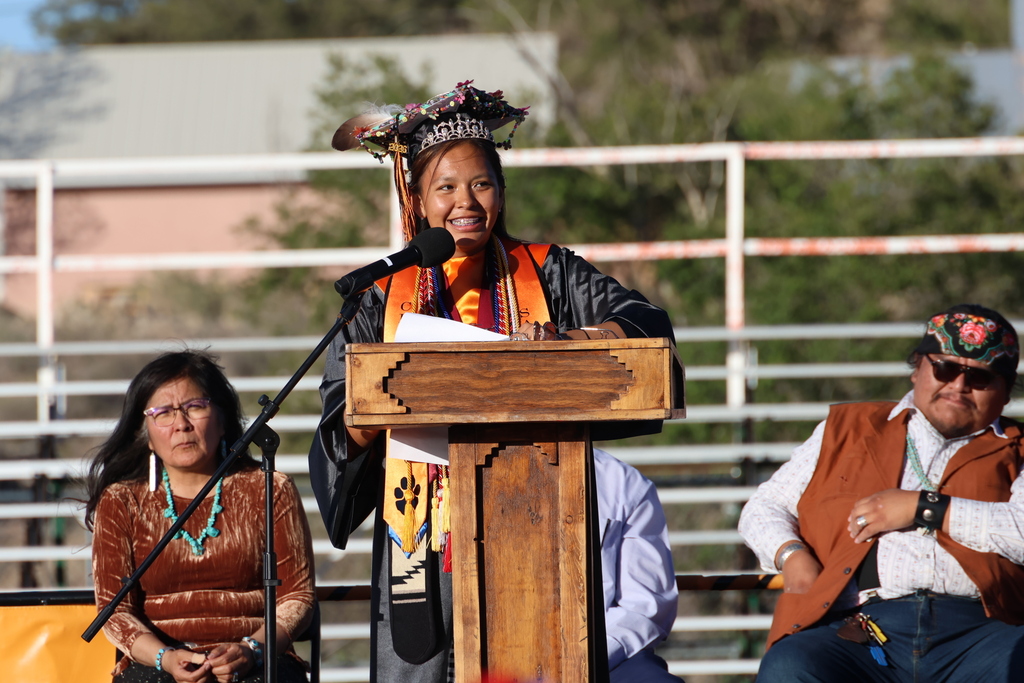 A woman speaks at a podium with a microphone while another woman and a man listen.