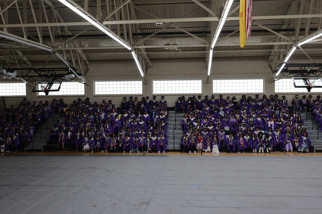 A large group of people in purple robes seated in tiered bleachers of a gymnasium.