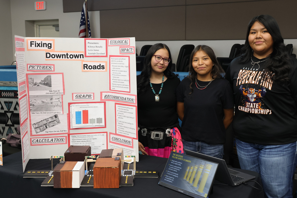 Four people stand behind a table with a model of downtown roads and a presentation poster.