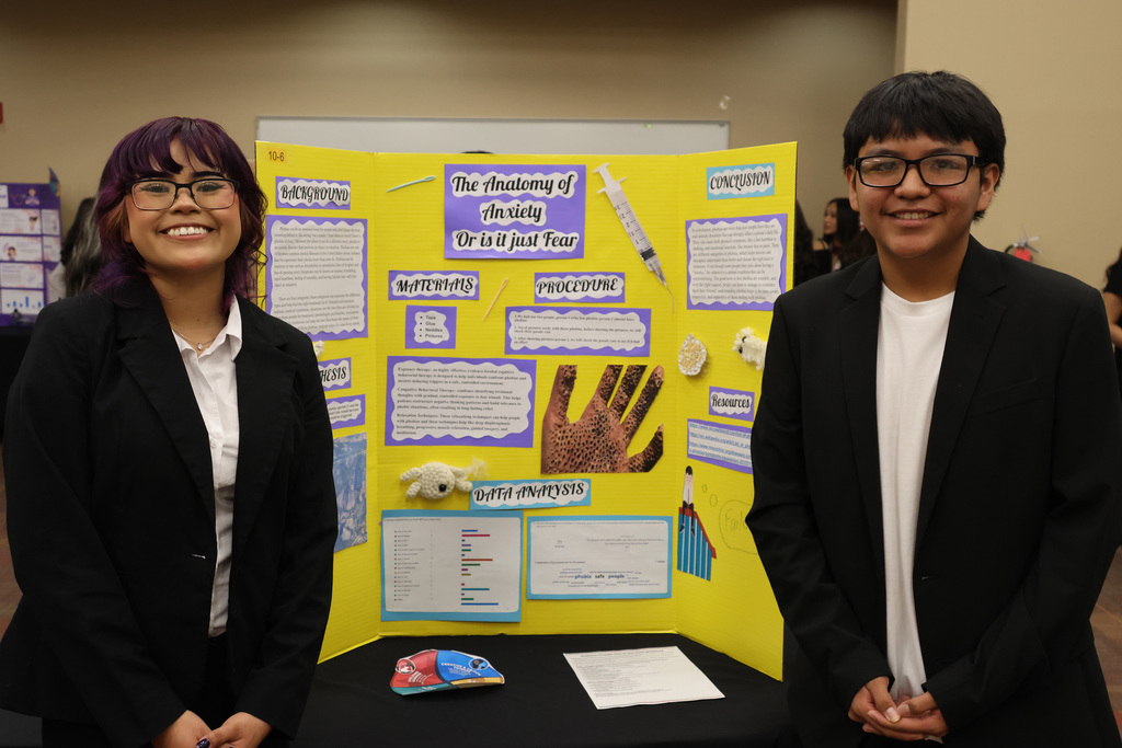 Two people in suits stand next to a yellow display board with a handprint and medical illustrations.