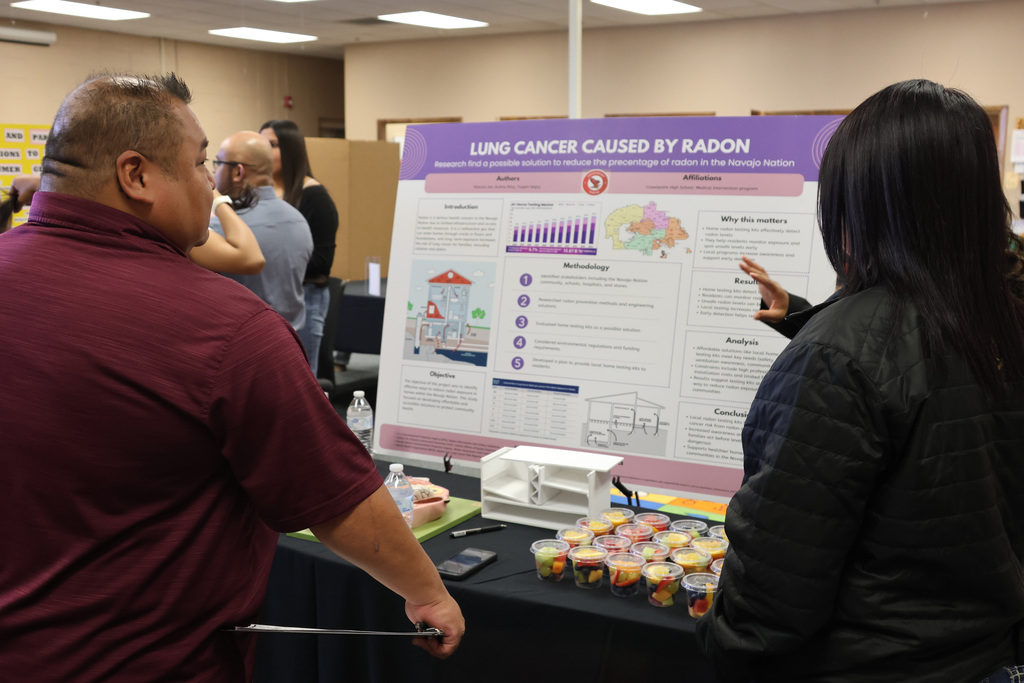 People examine a poster with text reading Lung Cancer Caused by Radon, with illustrations and a table with snacks.