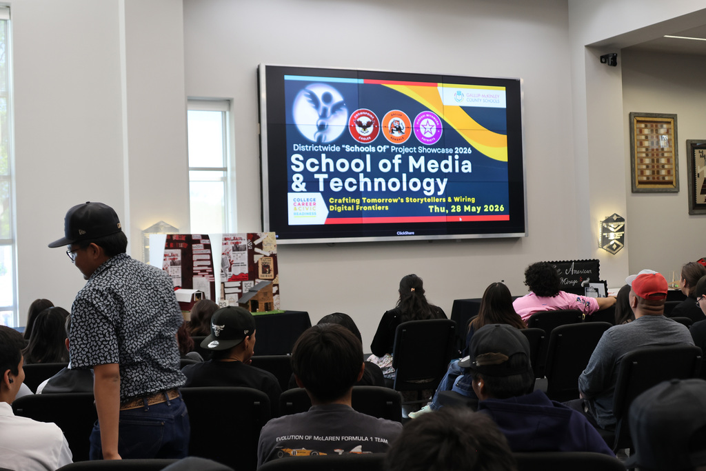A large screen displays "School of Media & Technology" above people in a classroom.
