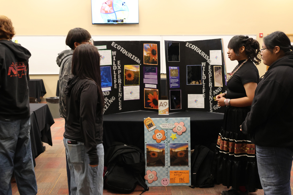 A group of people view a display of posters and pictures on a table in a room.