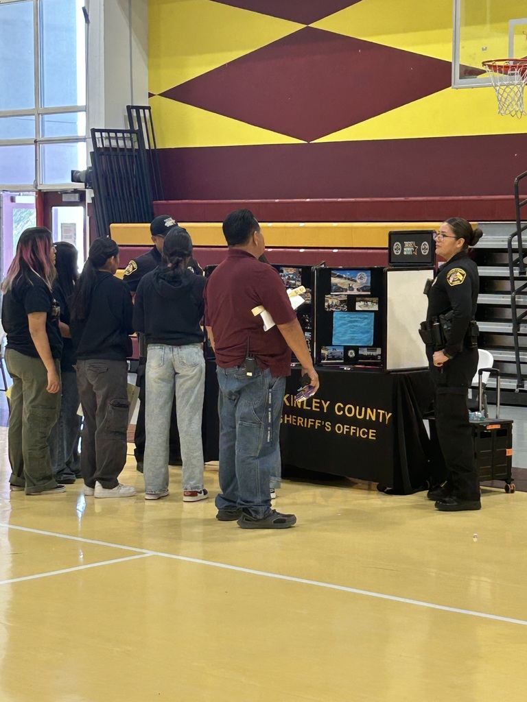People gather around a table with a monitor inside a gymnasium. A police officer stands nearby.