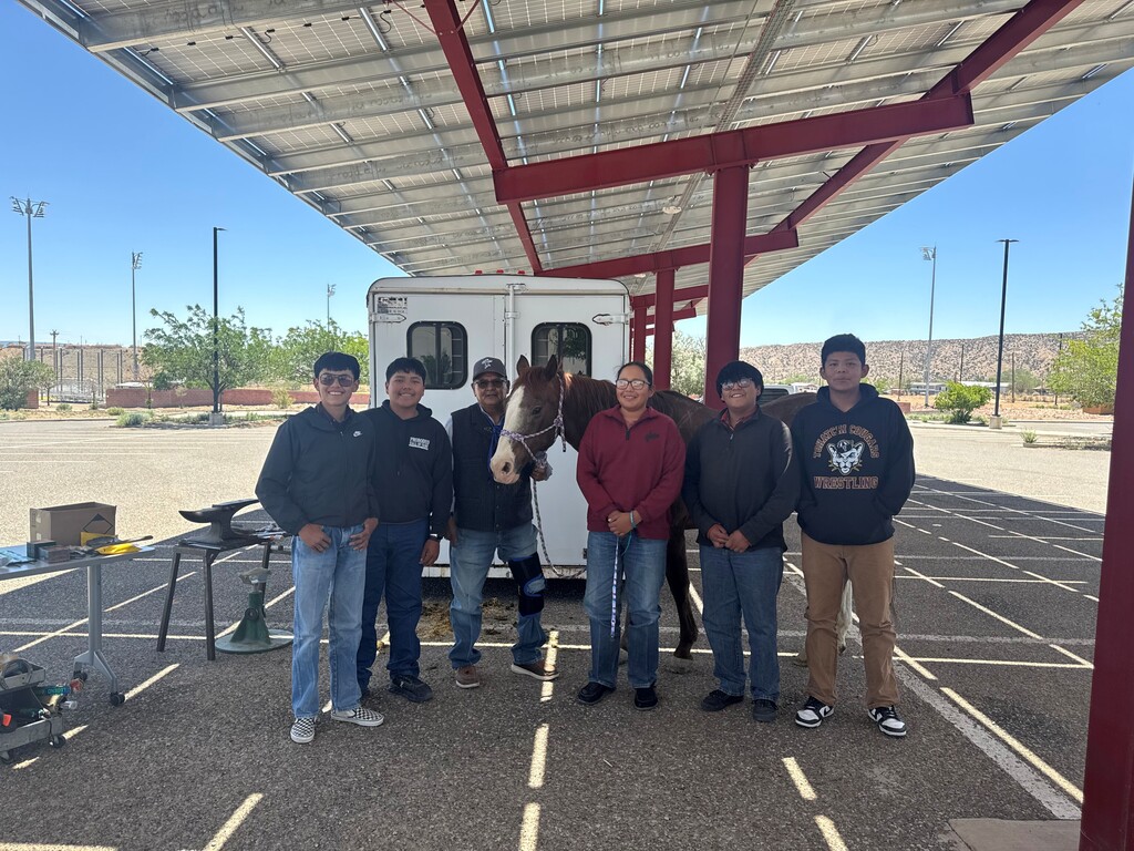 A group of students stand next to a horse in front of a horse trailer.