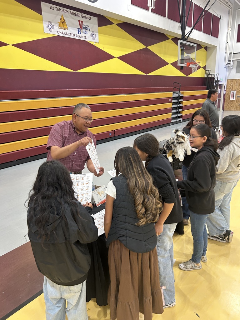 A group of people gathered around a table inside a gymnasium. One person at the table is speaking.
