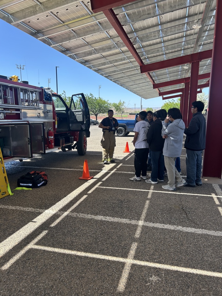 Fire truck parked, a person speaks to a group of people in a covered parking area.