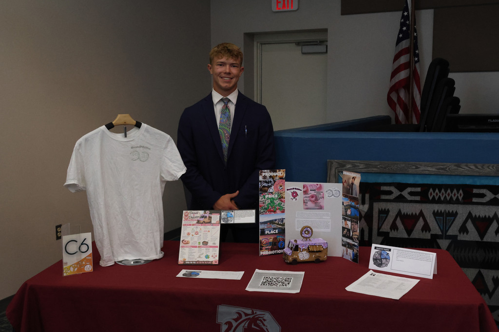 Man in suit and tie stands behind a table with a white shirt, calendars, and papers.