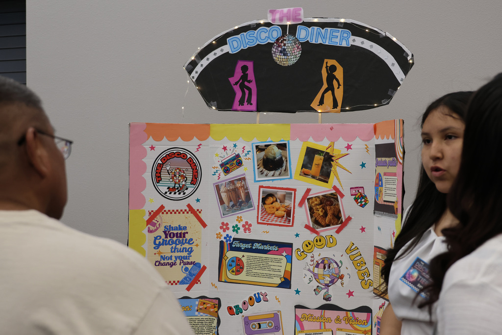 A man with glasses and a woman examine a colorful board with various pictures and a disco diner sign.