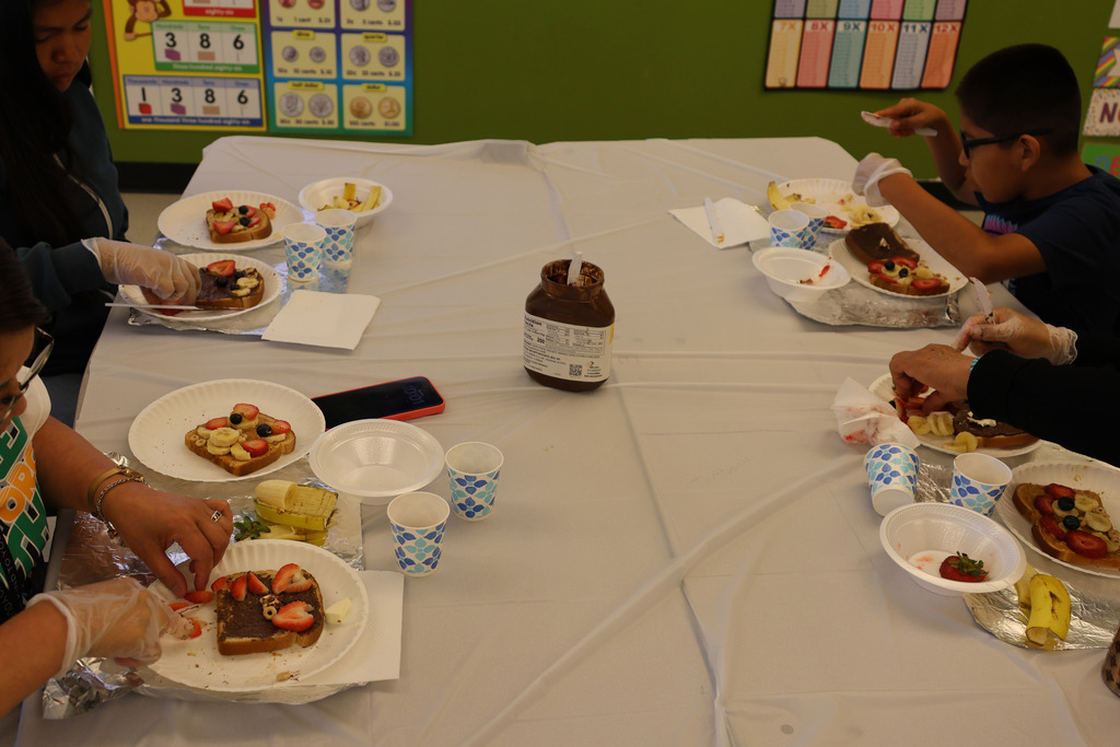 A group of people at a table, each with plates of food, including sandwiches and fruit.