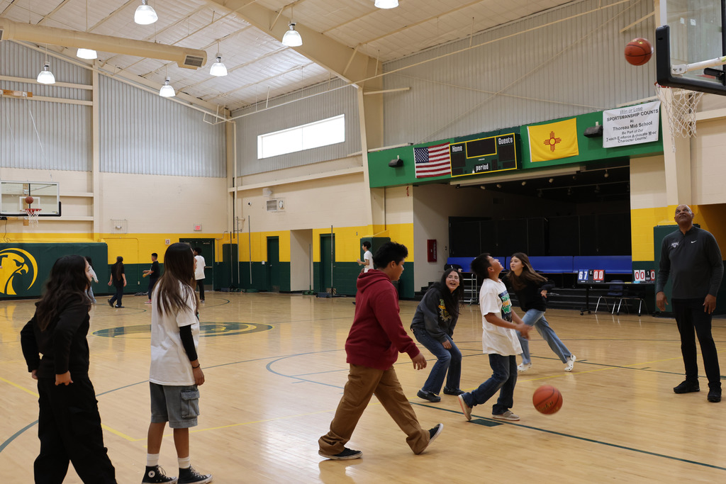 A group of people playing basketball in an indoor court. The floor is wooden.
