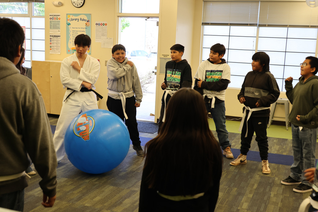 Group of students, some in martial arts uniforms, in a room with a blue exercise ball.