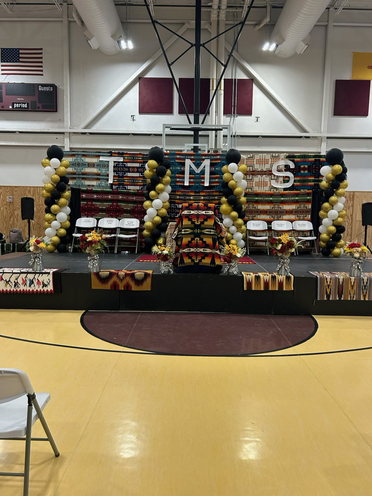 Decorated stage with balloons and a flag at the back in an indoor basketball court.