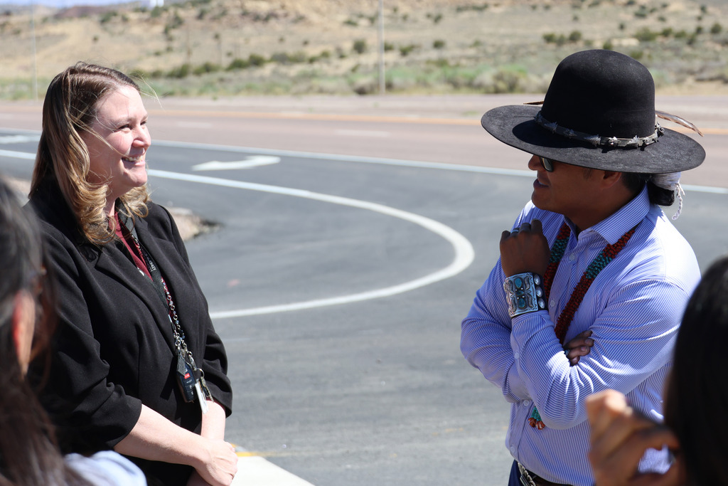 People stand outside with a desert landscape in the background. A man and a woman converse.