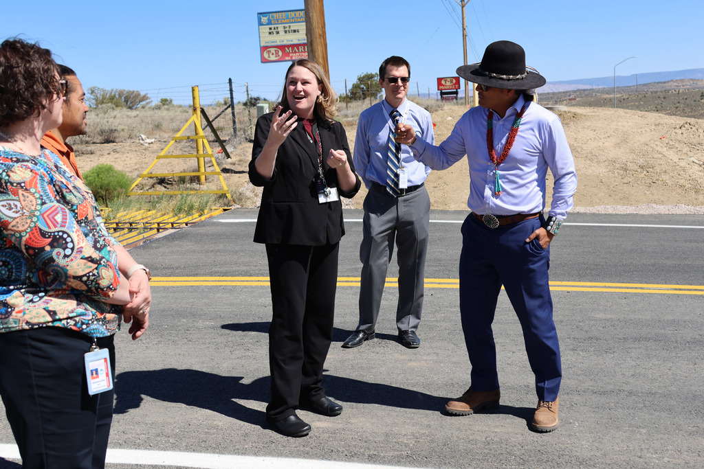 Four people stand in an intersection. The person on the left wears a colorful blouse. A woman in black speaks to the man in blue.