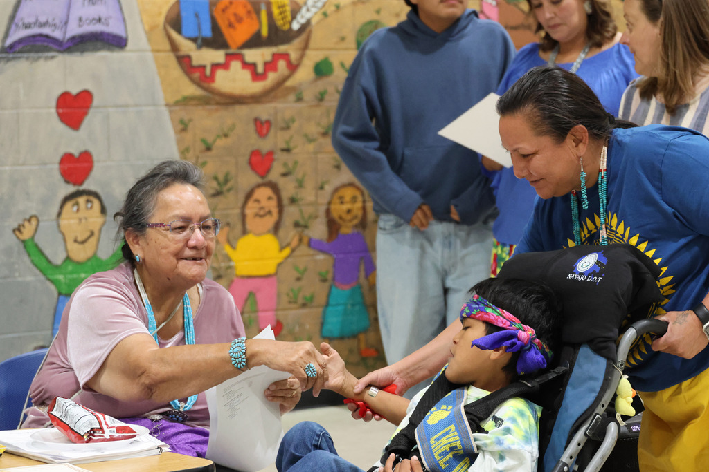 Several people in a room with a mural. A woman in a wheelchair shakes hands with a smiling woman.