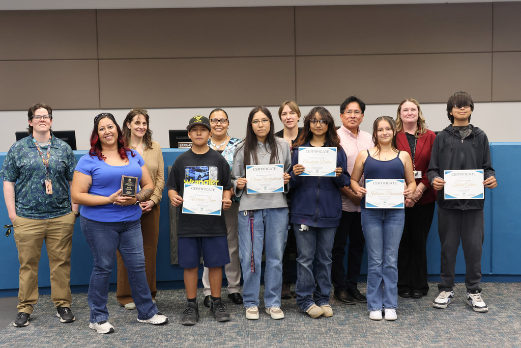 A group of individuals stands in a line, smiling, holding certificates. The wall behind them is blue.