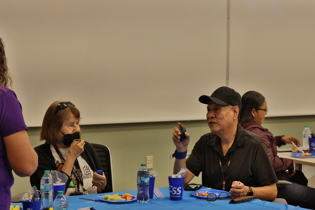 Group sitting at a table in a classroom, with blue tablecloth and various items on it.