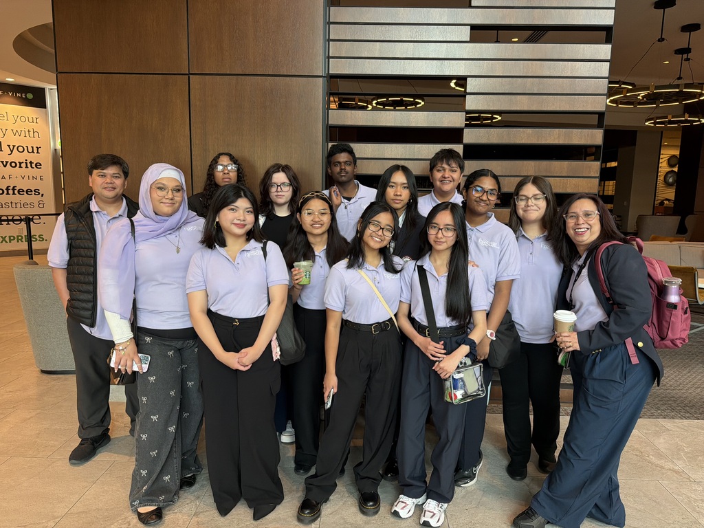 A group of individuals in matching purple shirts stand in a lobby, smiling and posing for a photo.