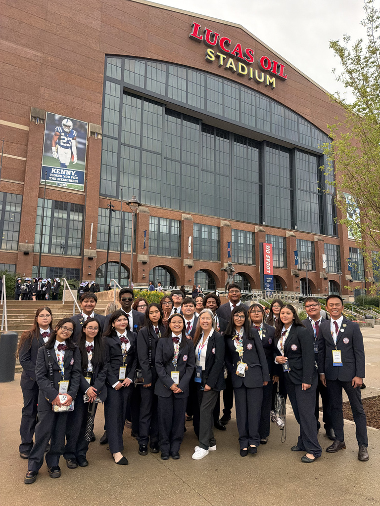 Group of students in suits pose for a photo in front of Lucas Oil Stadium.