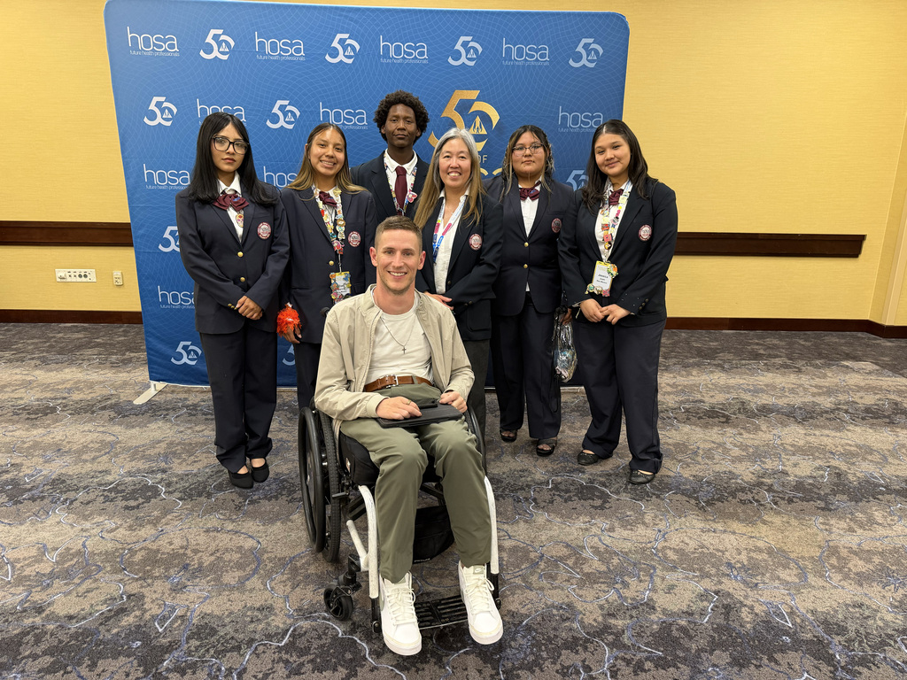 Seven people, including one in a wheelchair, pose for a photo in front of a blue banner.
