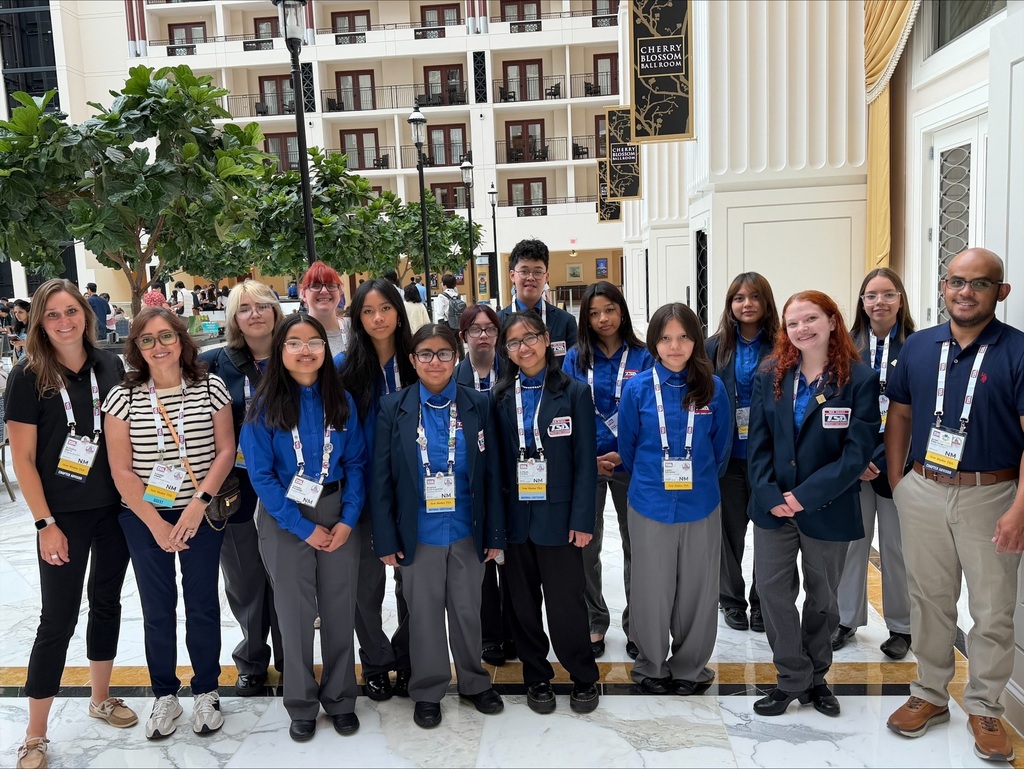 Group of students in blue shirts, some with IDs, posing in front of a building with balconies.