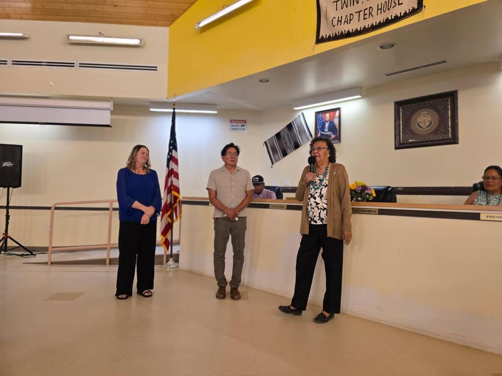 Four people stand in a room with an American flag. A woman holds a microphone. A banner says "Tampa Chapter House".