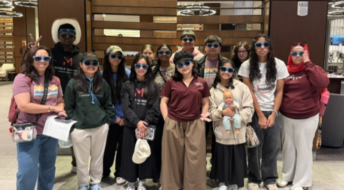 A group of people wearing sunglasses and various clothing, standing together indoors near a wall.