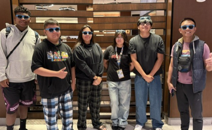 Six people in matching sunglasses stand next to each other in front of a wooden wall.