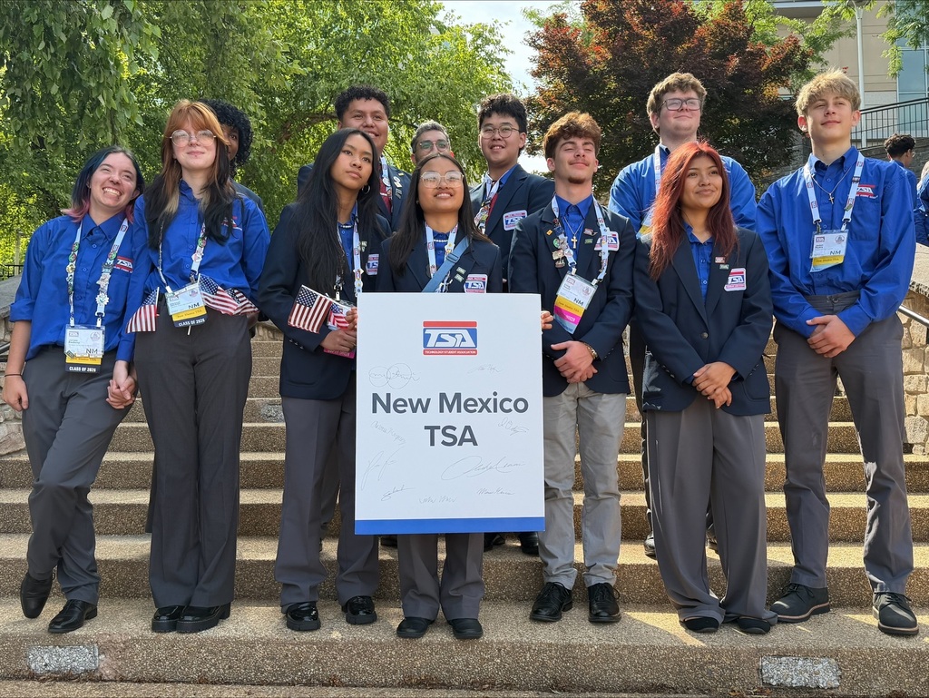 A group of young people in blue shirts and gray pants pose for a photo on stairs.