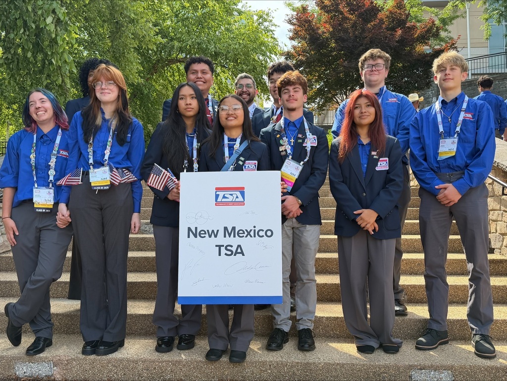 Group of individuals wearing blue uniforms with "TSA" on the back, standing on steps, holding signs.