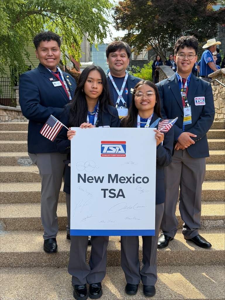 Five students in blazers stand on stairs, holding flags and a sign reading "New Mexico TSA." Trees and buildings in the background.
