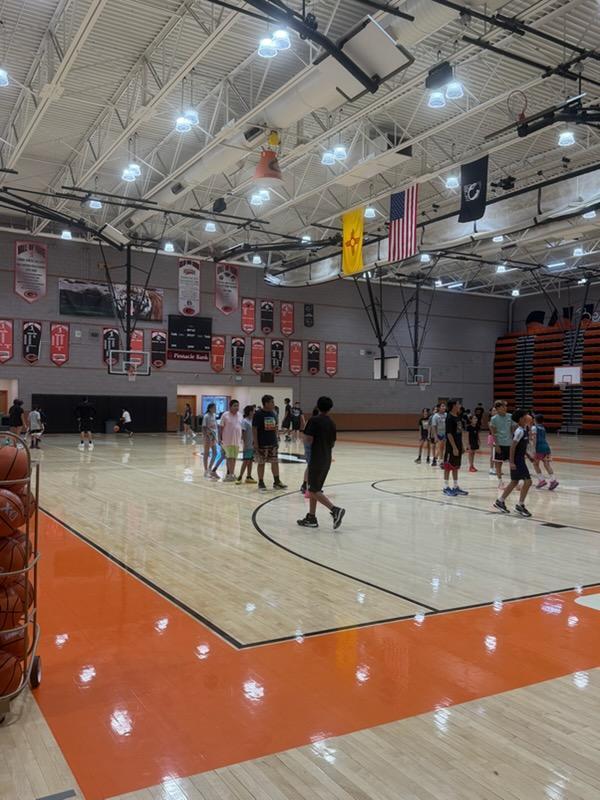 An indoor basketball court with multiple individuals engaged in activities. The floor is wooden, and flags are hung on the walls.