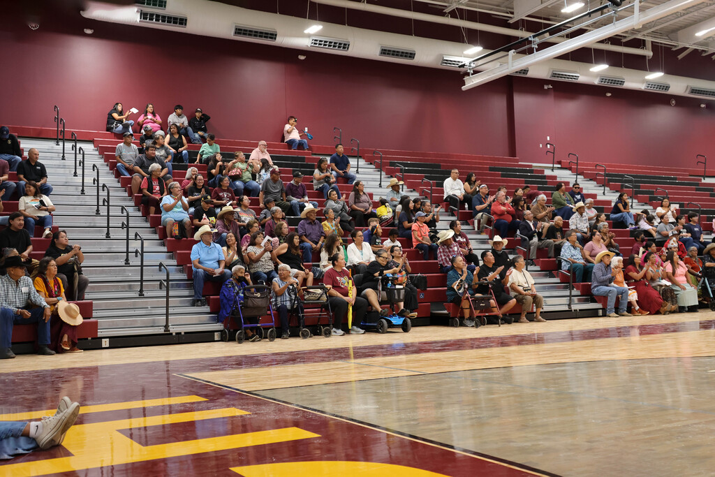 A basketball court with many people sitting on the red bleachers in an indoor arena.
