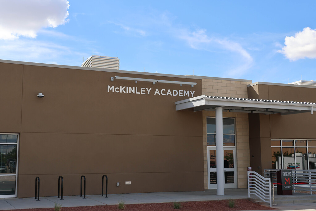 A brown building named McKinley Academy with glass doors, a small awning, and a sidewalk with bike racks.