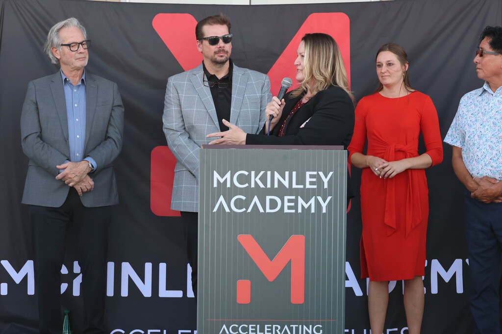 People stand at a podium with a sign reading "McKinley Academy" in front of a backdrop.