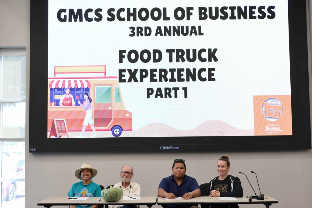 Four people seated at a table with microphones, facing a screen that displays a food truck graphic.