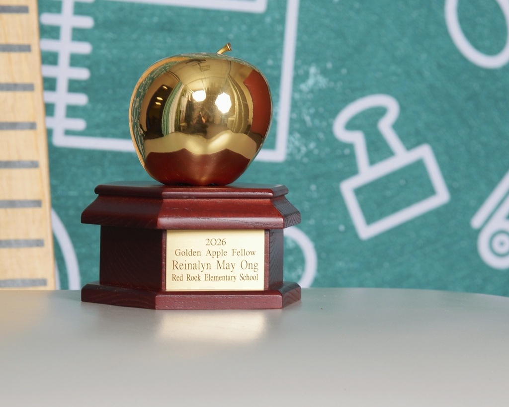 A golden apple trophy rests on a wooden base with a plaque inscribed "2005 Golden Apple Fellow, Kinshay May Orr, Rd. Kich Elementary School".